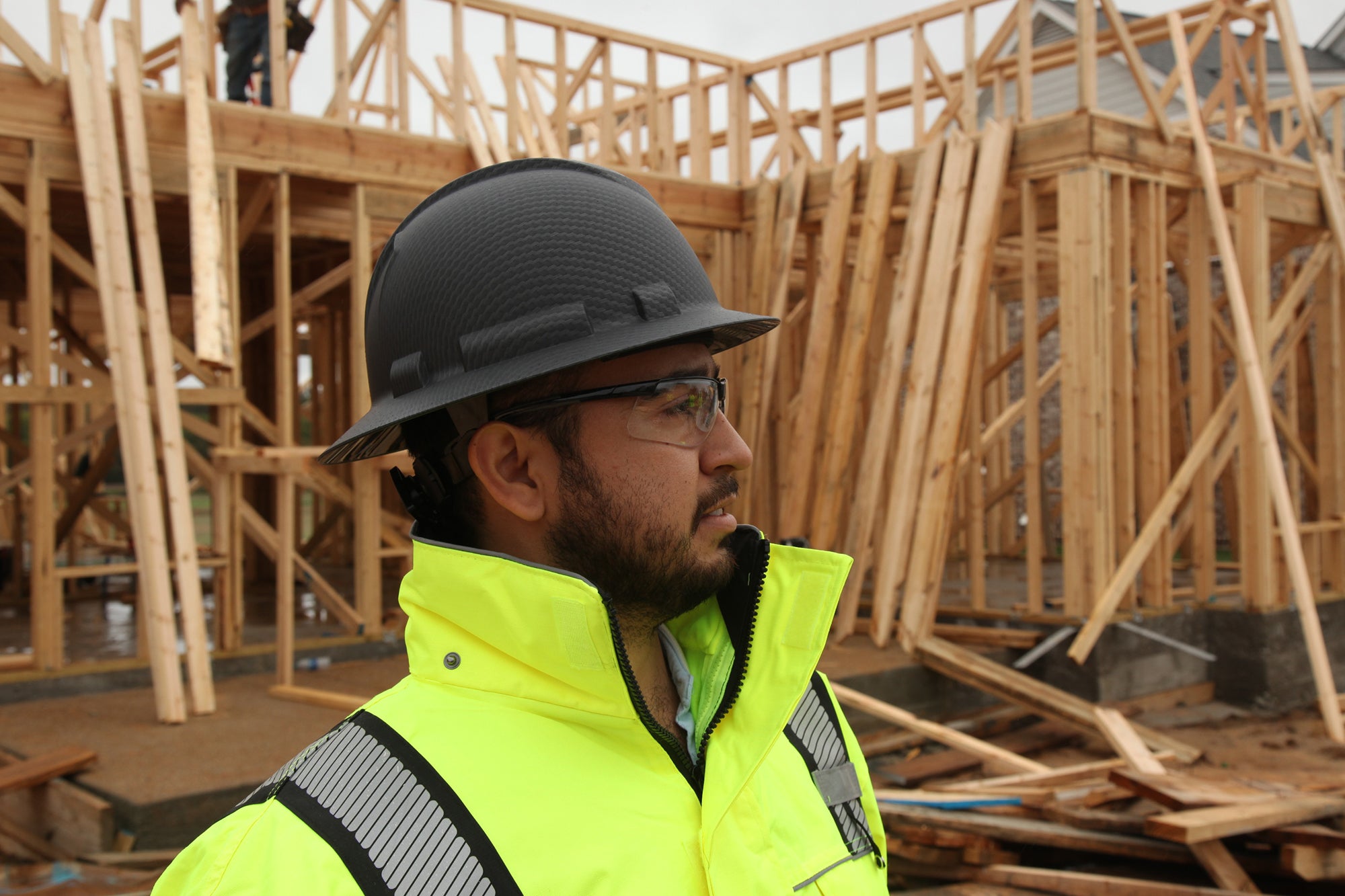 Worker surveying site wearing Ridgeline full brim hard hat, Ever-lite safety eyewear, and work wear jacket.