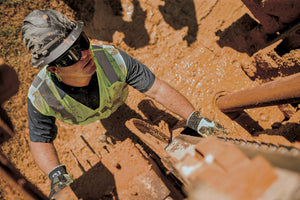 Oil worker wearing a Ridgeline Full Brim hard hat, earplugs, hi-vis work wear, synthetic gloves, and sealed eyewear.